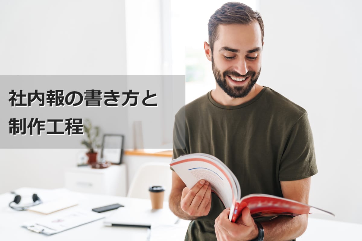 Image of caucasian happy man wearing casual t-shirt reading brochure and smiling while working in bright office
